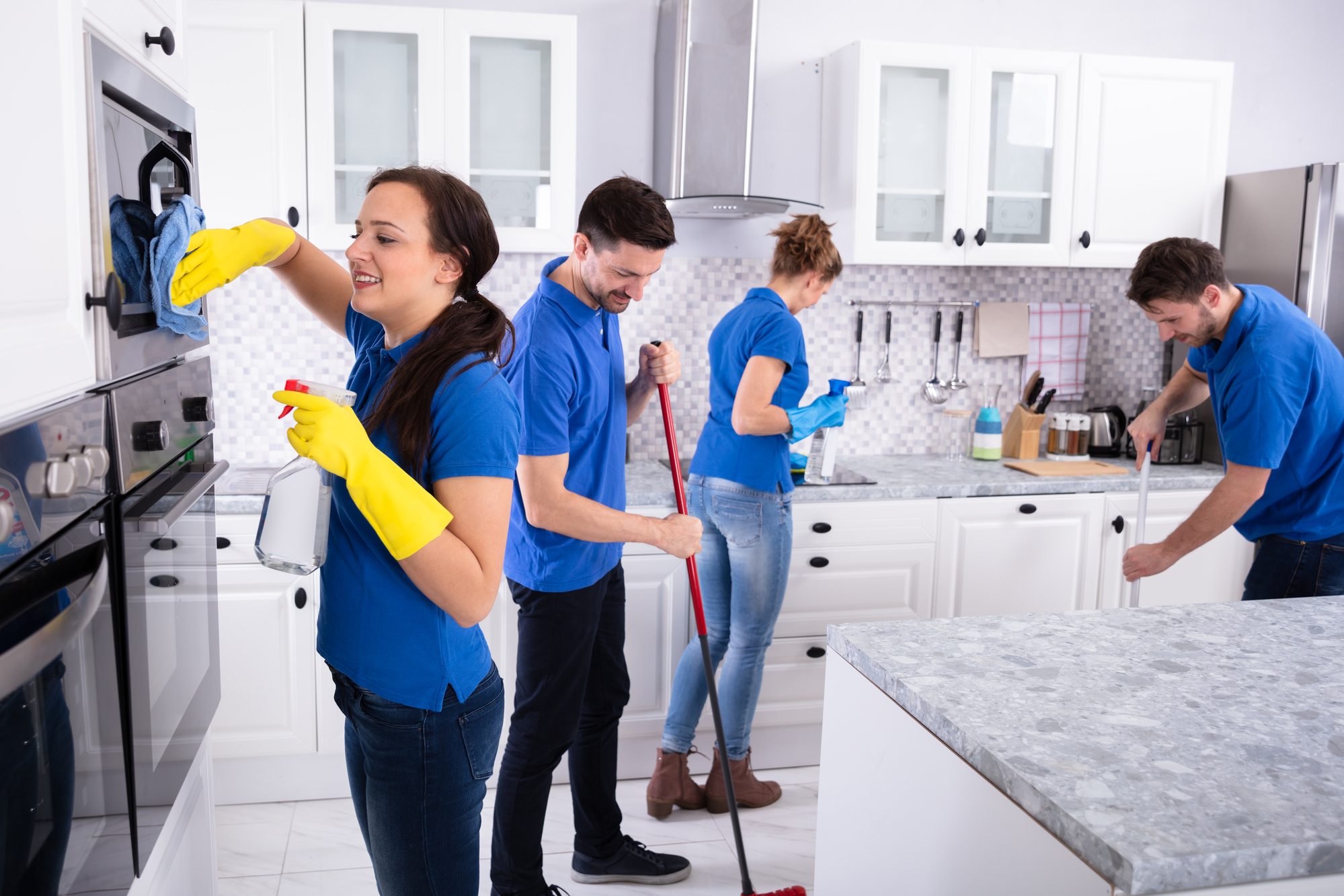 Group Of Young Janitors In Uniform Cleaning Kitchen At Home